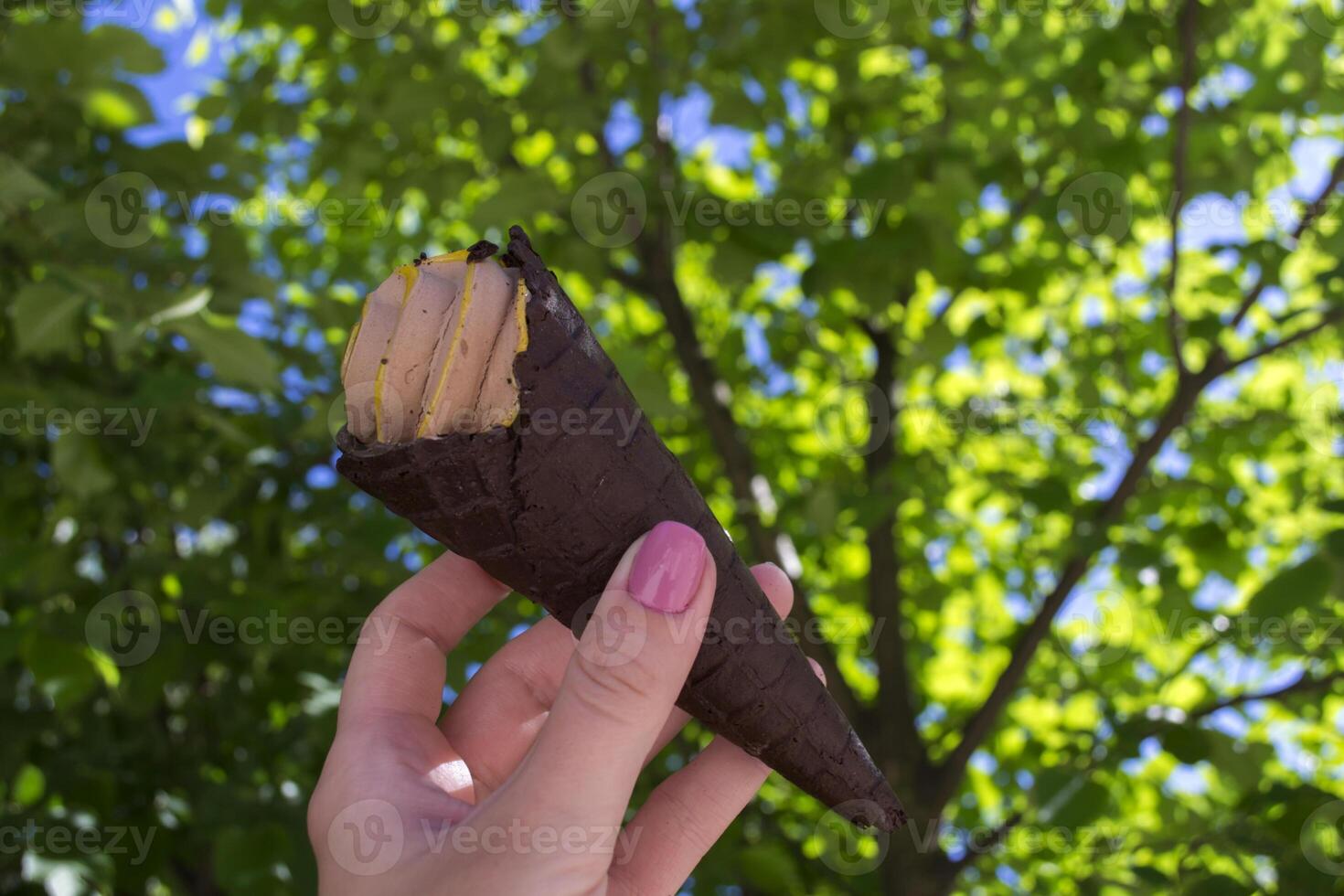 An ice cream cone in female arm against a green tree background photo