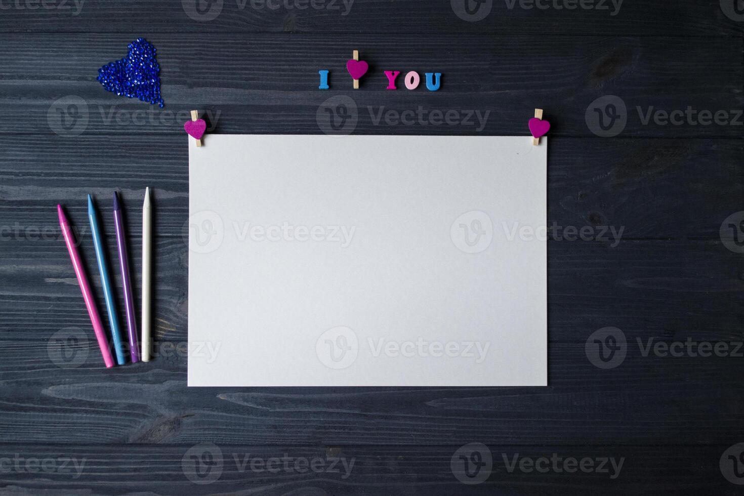 White paper, colorful pencils and decor on a blue wooden background. Greeting card photo