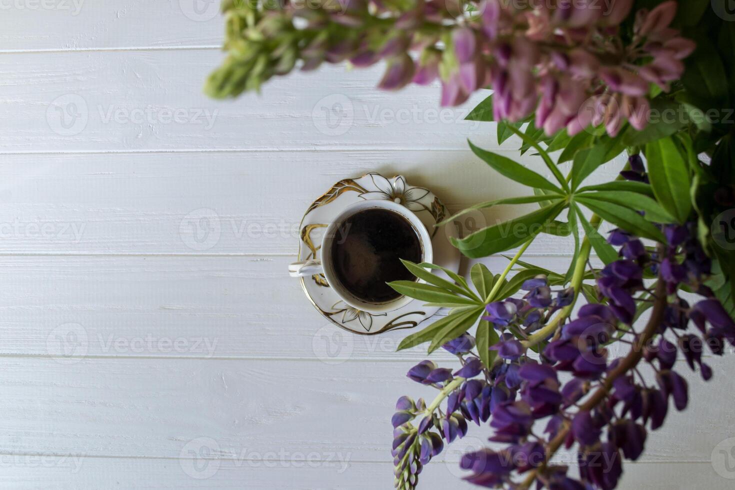 A cup of coffee and lupine flowers on a white wooden table. photo