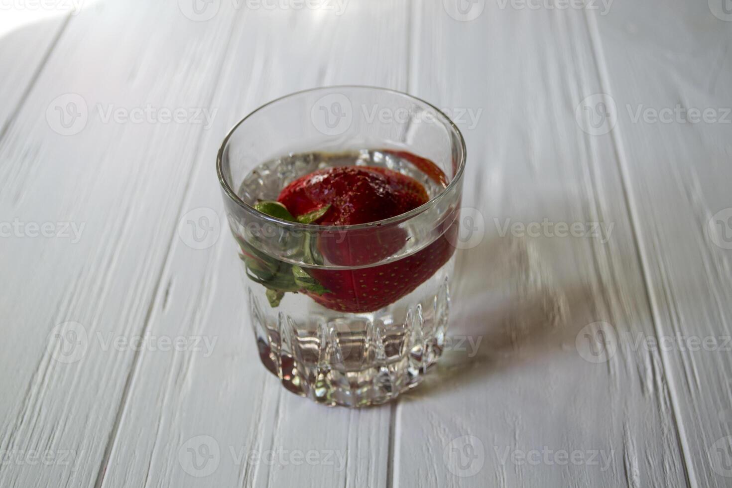 Ripe strawberry in a glass with water on a white wooden table. photo