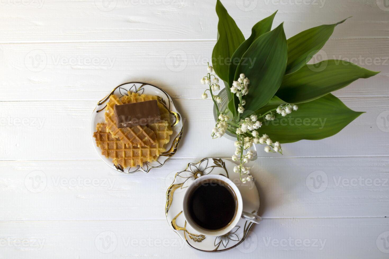 Lily of the valley, a cup of coffee and dessert on a white wooden table. photo