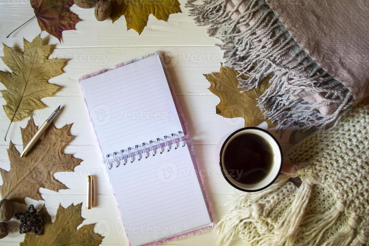 The notepad, warm scarves, autumn leaves and hot tea on the white wooden desk. Autumn background with copy space. photo