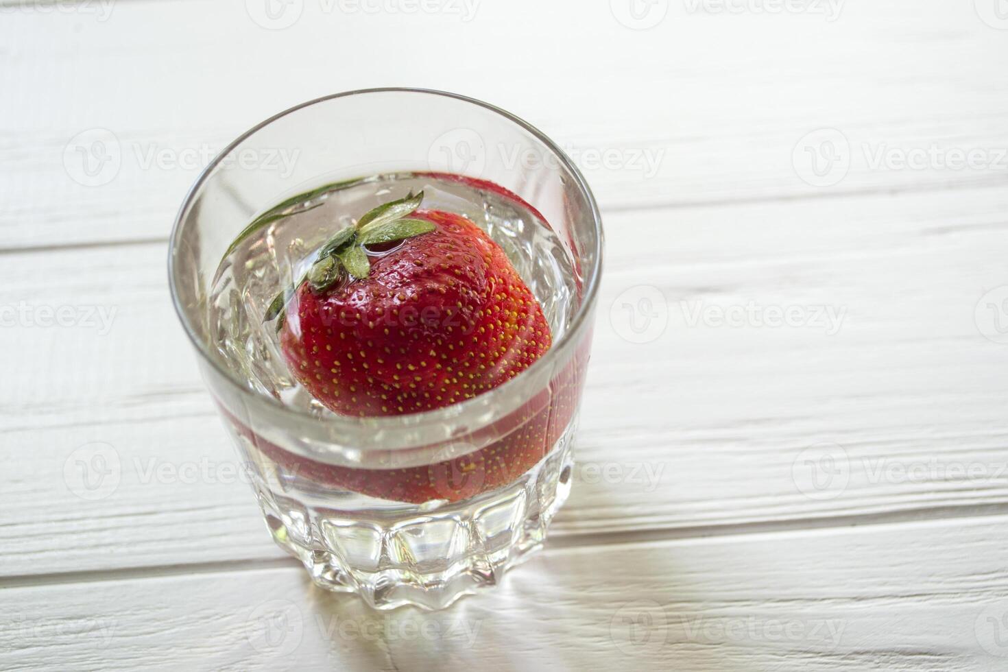 maduro fresa en un vaso con agua en un blanco de madera mesa. foto