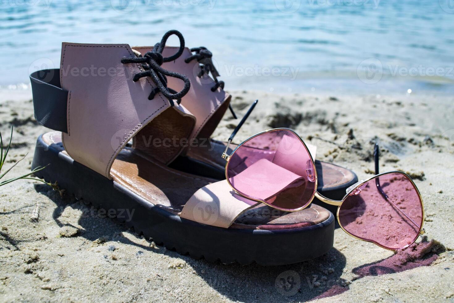 Female shoes and pink glasses on the coast of blue lake. photo