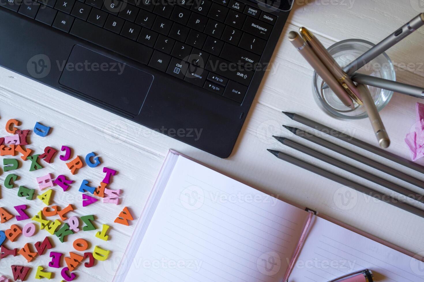 A tablet, notebook, pencils and multicolor letters on a white wooden desk. Desktop top view. photo