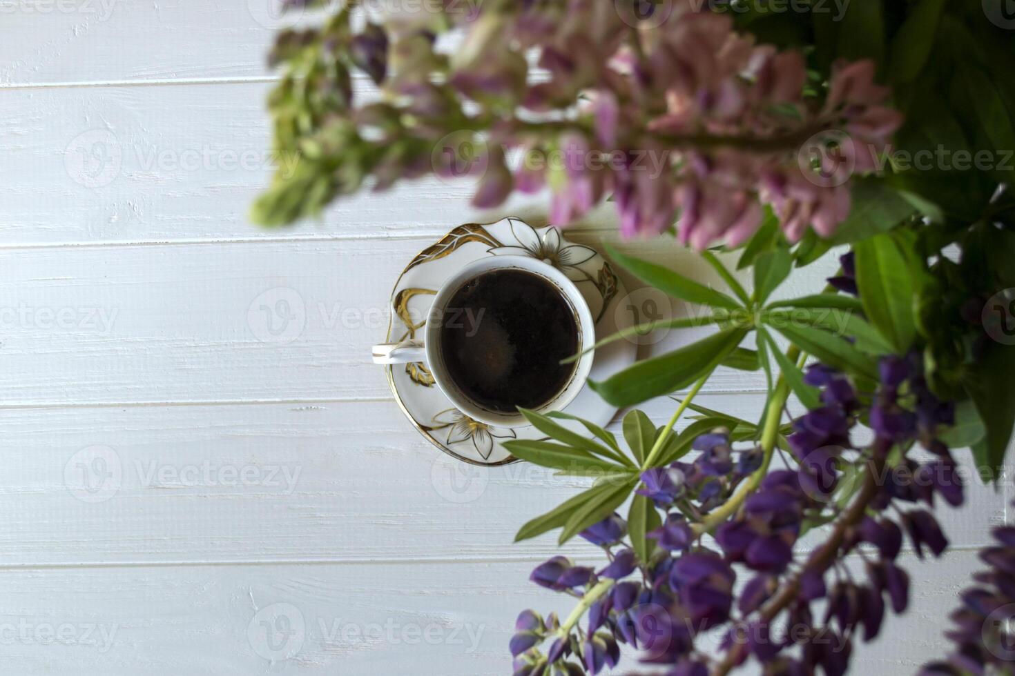 A cup of coffee and lupine flowers on a white wooden table. photo