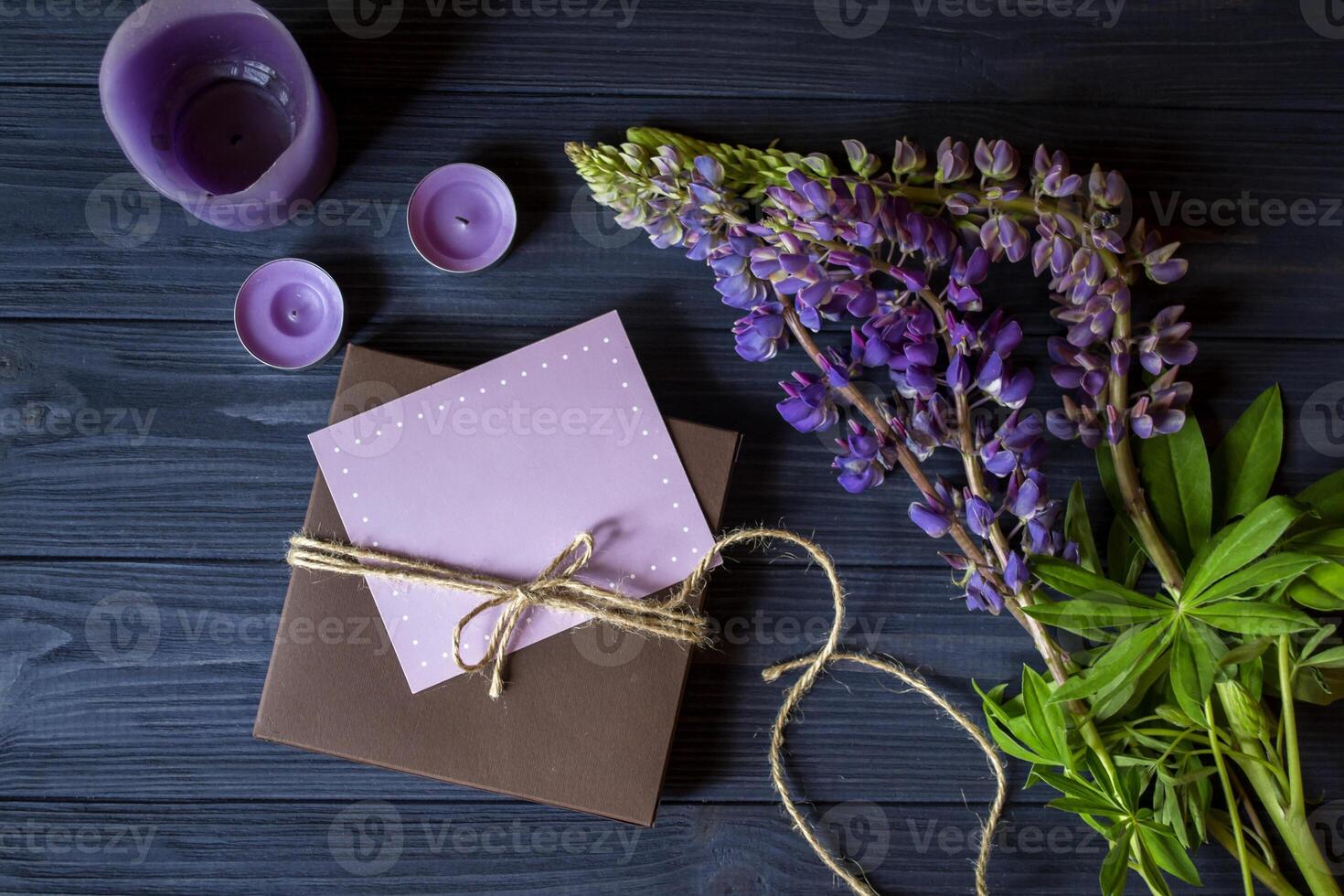 Gift box with greeting card and bouquet of lupins on a dark blue wooden background. photo