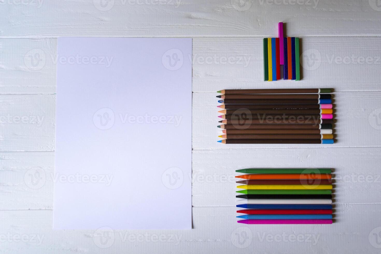 Palette of multicolored pencils and the sheet of white paper on a white wooden desk. photo