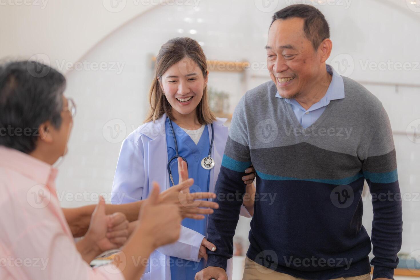 Asian young nurse support senior older man walk with walker. Beautiful nurse help and take care. elderly mature grandpa patient doing physical therapy with a group of senior friends in hospital. photo