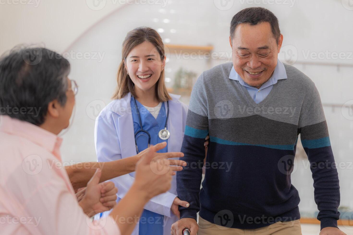 Asian young nurse support senior older man walk with walker. Beautiful nurse help and take care. elderly mature grandpa patient doing physical therapy with a group of senior friends in hospital. photo