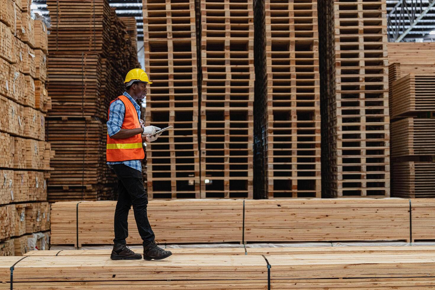 African workers man engineering walking and inspecting with working suite dress and hand glove in timber wood warehouse. Concept of smart industry worker operating. Wood factories produce wood palate. photo