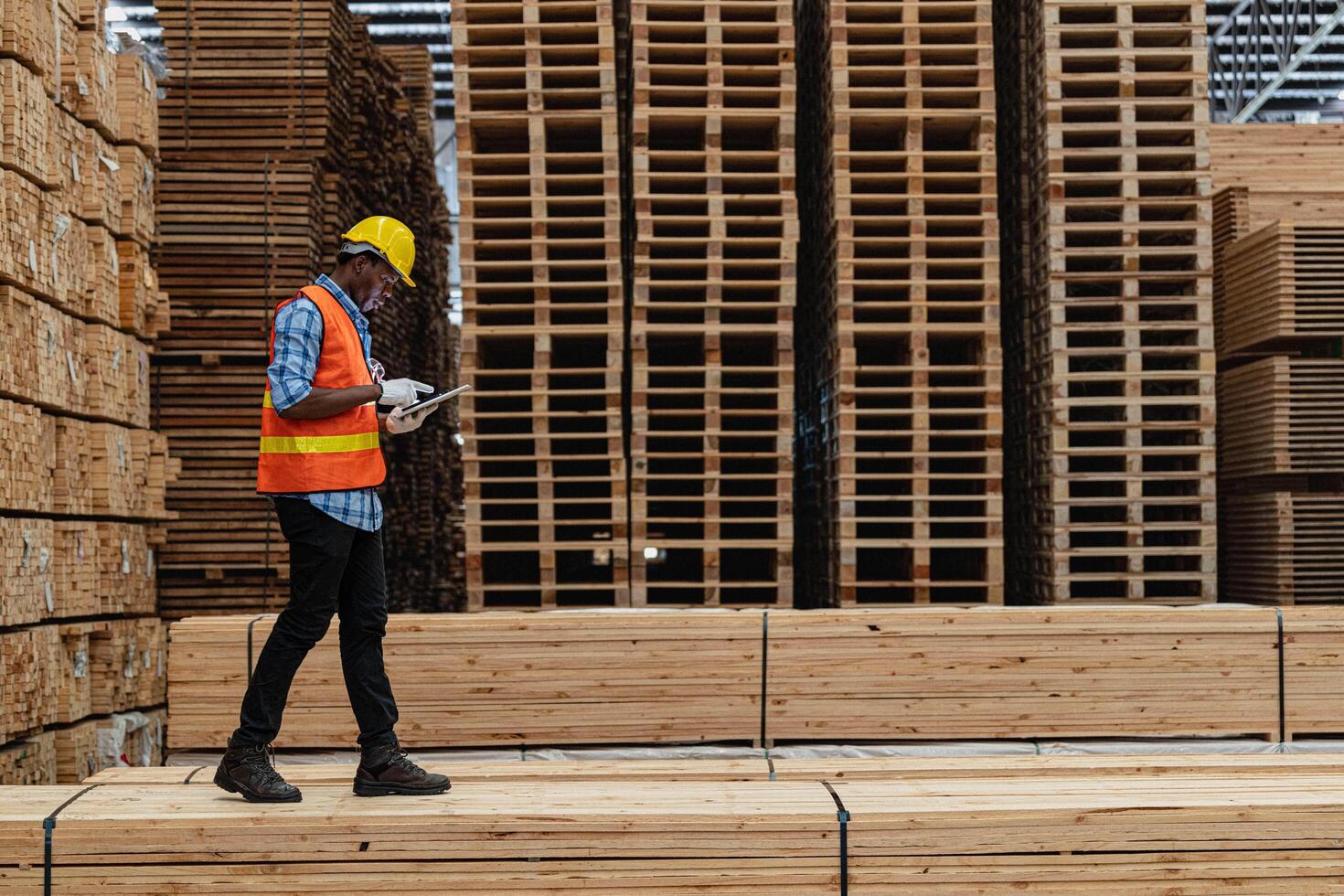 African workers man engineering walking and inspecting with working suite dress and hand glove in timber wood warehouse. Concept of smart industry worker operating. Wood factories produce wood palate. photo