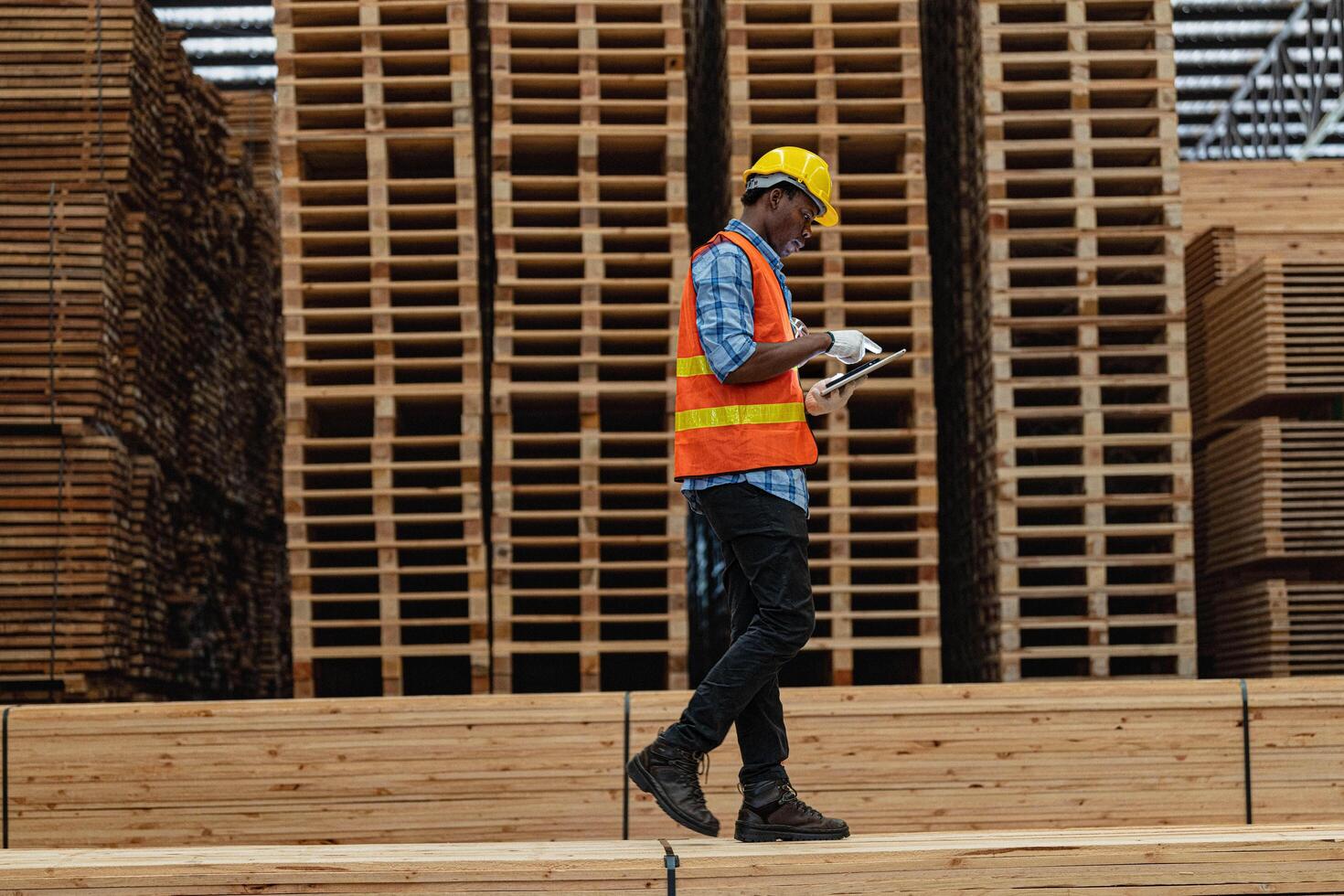 African workers man engineering walking and inspecting with working suite dress and hand glove in timber wood warehouse. Concept of smart industry worker operating. Wood factories produce wood palate. photo