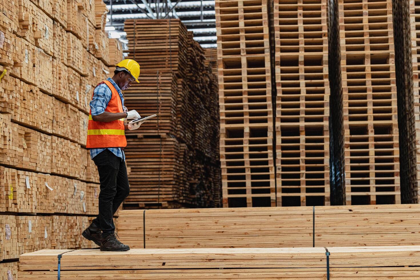 African workers man engineering walking and inspecting with working suite dress and hand glove in timber wood warehouse. Concept of smart industry worker operating. Wood factories produce wood palate. photo