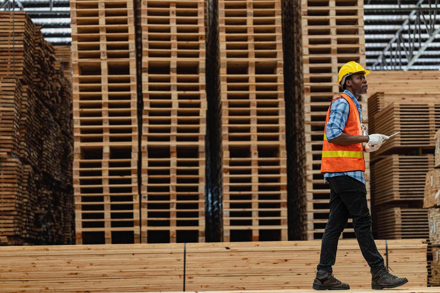 African workers man engineering walking and inspecting with working suite dress and hand glove in timber wood warehouse. Concept of smart industry worker operating. Wood factories produce wood palate. photo