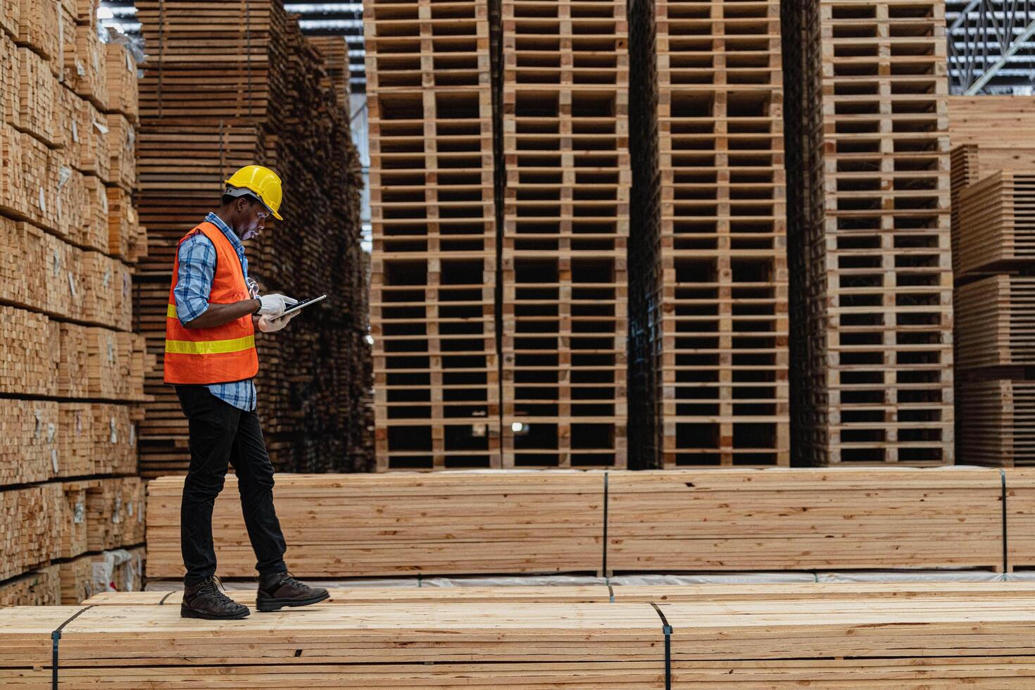 African workers man engineering walking and inspecting with working suite dress and hand glove in timber wood warehouse. Concept of smart industry worker operating. Wood factories produce wood palate. photo