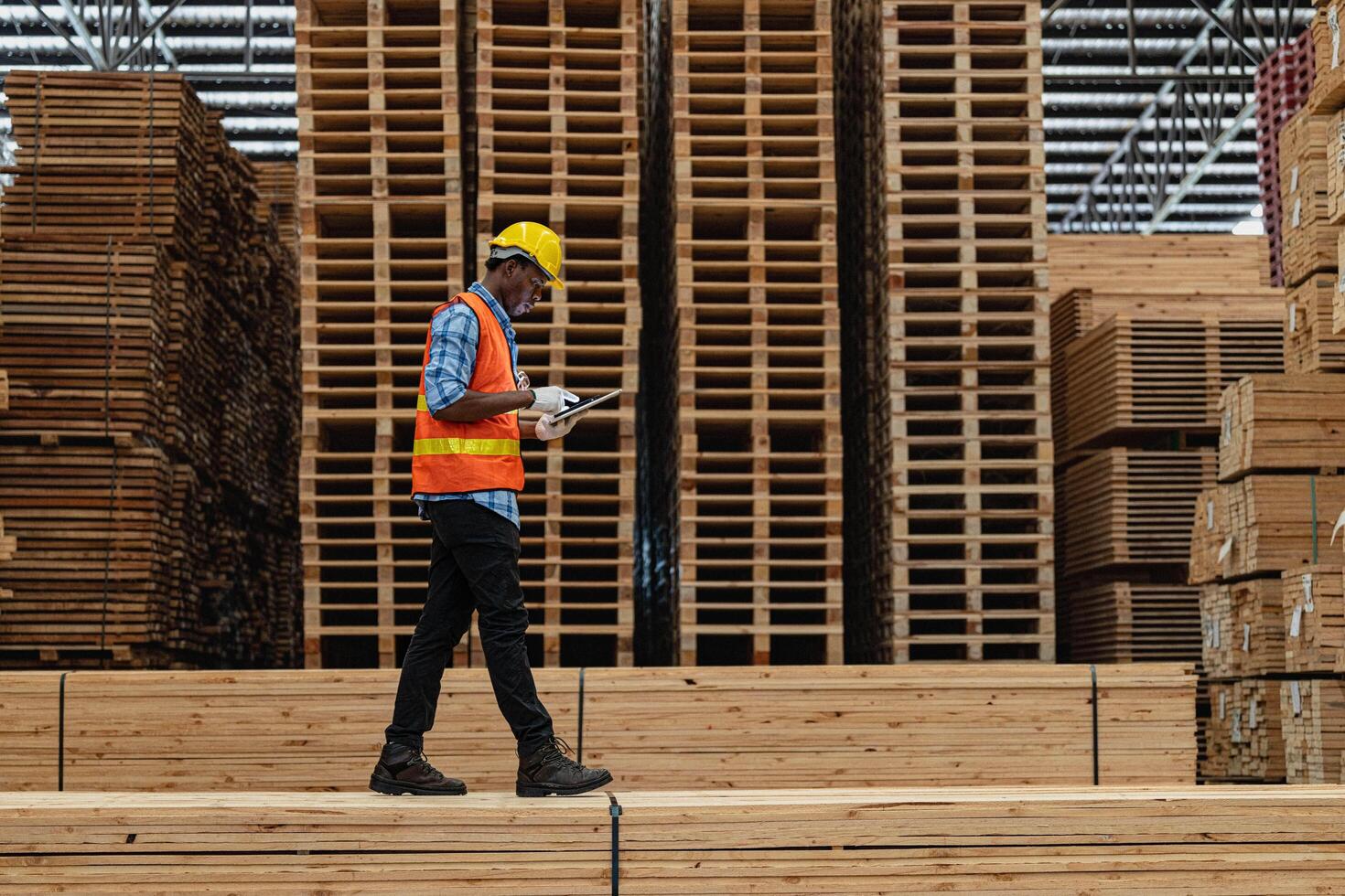 African workers man engineering walking and inspecting with working suite dress and hand glove in timber wood warehouse. Concept of smart industry worker operating. Wood factories produce wood palate. photo