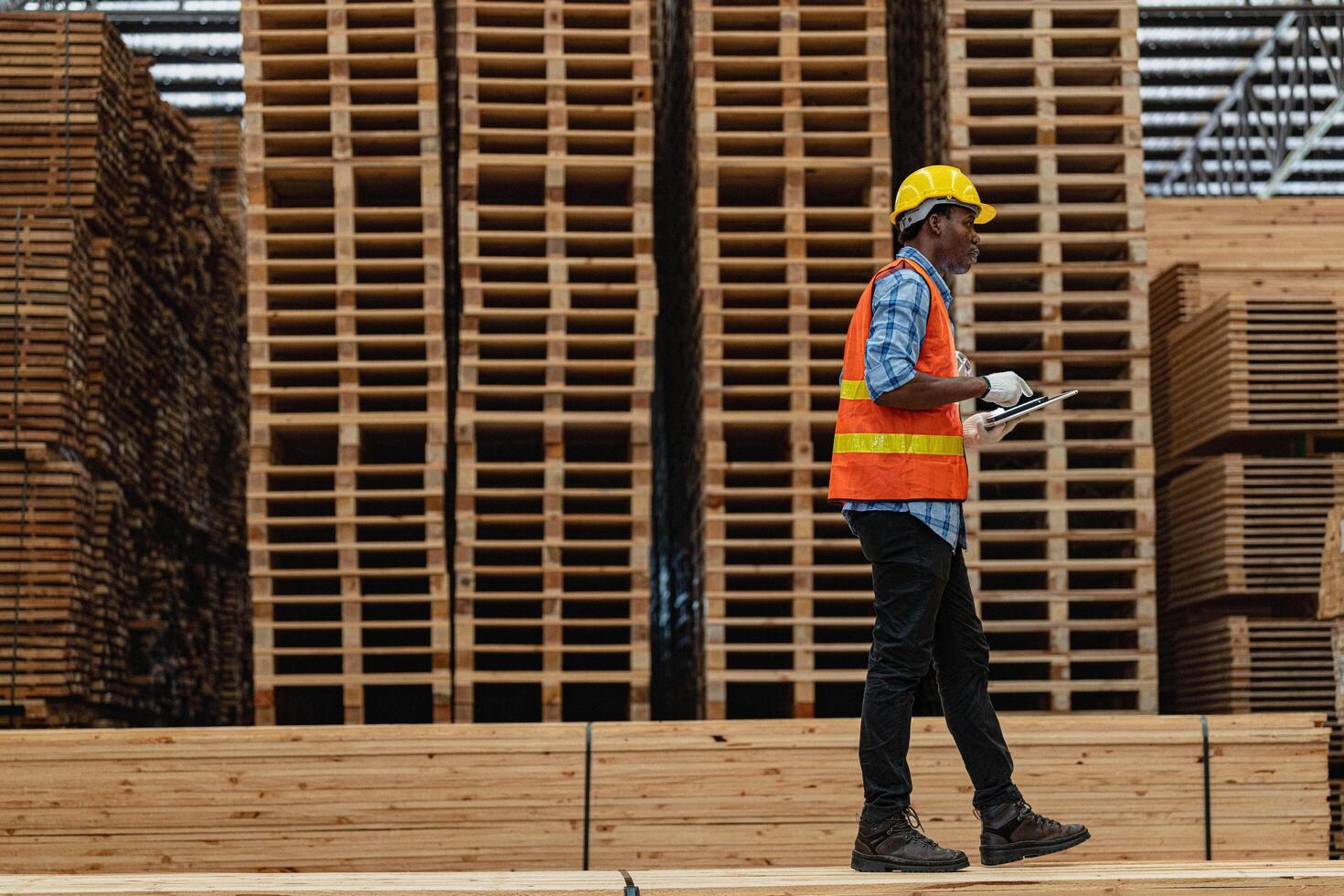 African workers man engineering walking and inspecting with working suite dress and hand glove in timber wood warehouse. Concept of smart industry worker operating. Wood factories produce wood palate. photo