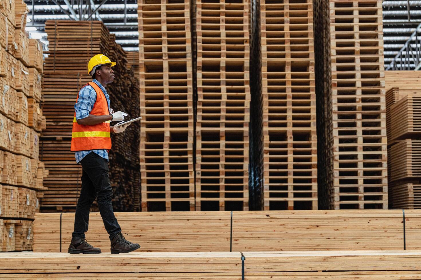 African workers man engineering walking and inspecting with working suite dress and hand glove in timber wood warehouse. Concept of smart industry worker operating. Wood factories produce wood palate. photo
