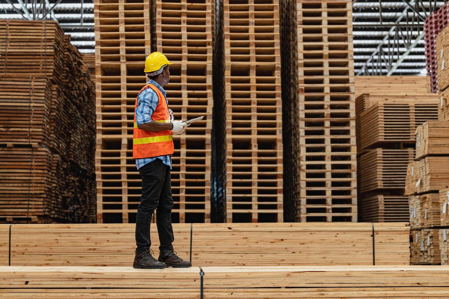 African workers man engineering walking and inspecting with working suite dress and hand glove in timber wood warehouse. Concept of smart industry worker operating. Wood factories produce wood palate. photo