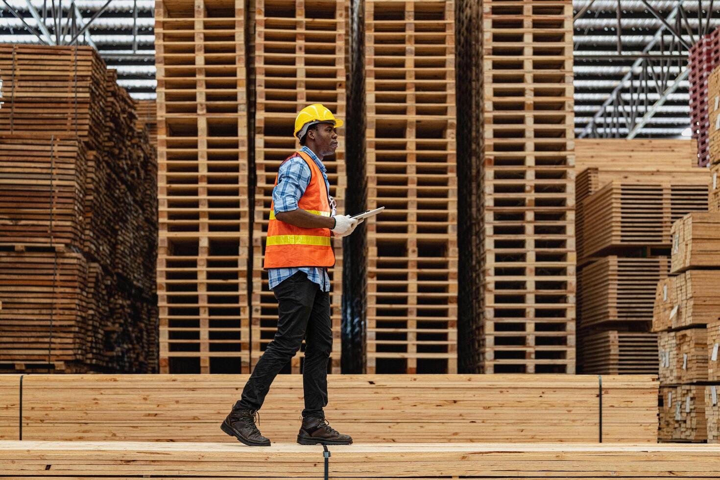 African workers man engineering walking and inspecting with working suite dress and hand glove in timber wood warehouse. Concept of smart industry worker operating. Wood factories produce wood palate. photo