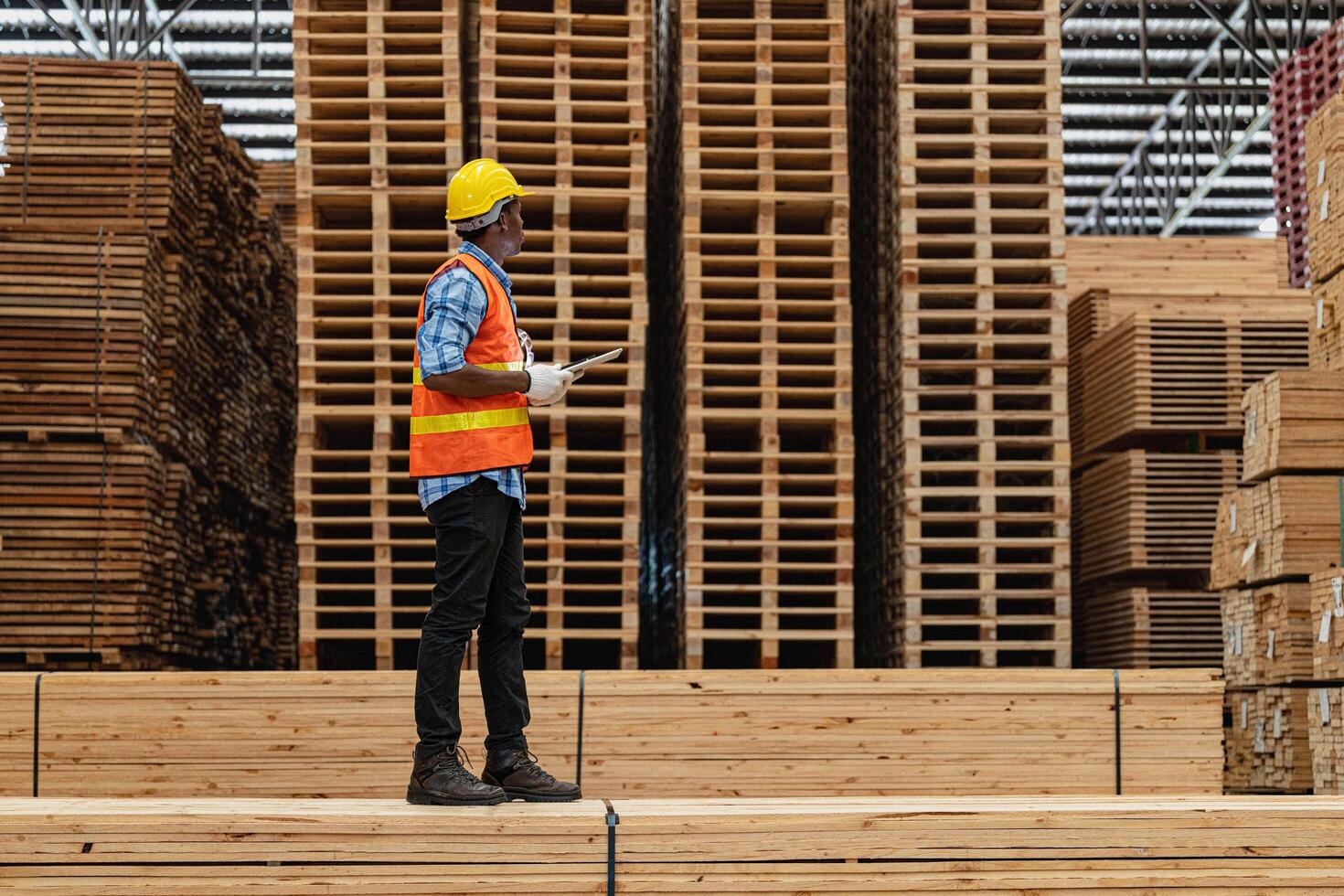 African workers man engineering walking and inspecting with working suite dress and hand glove in timber wood warehouse. Concept of smart industry worker operating. Wood factories produce wood palate. photo