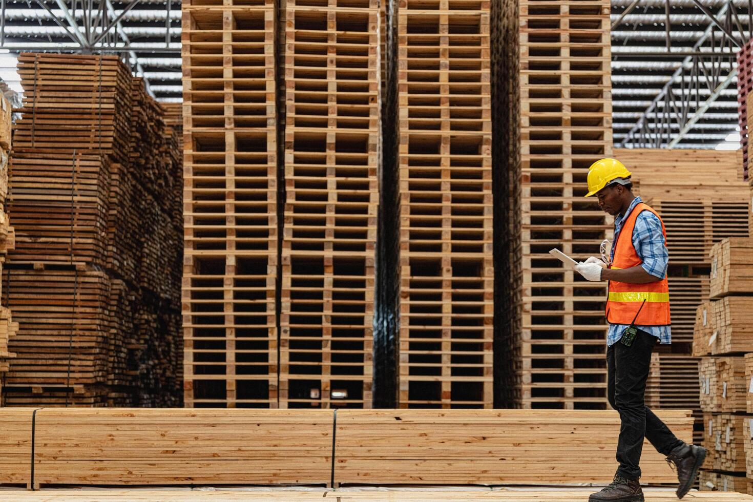 African workers man engineering walking and inspecting with working suite dress and hand glove in timber wood warehouse. Concept of smart industry worker operating. Wood factories produce wood palate. photo