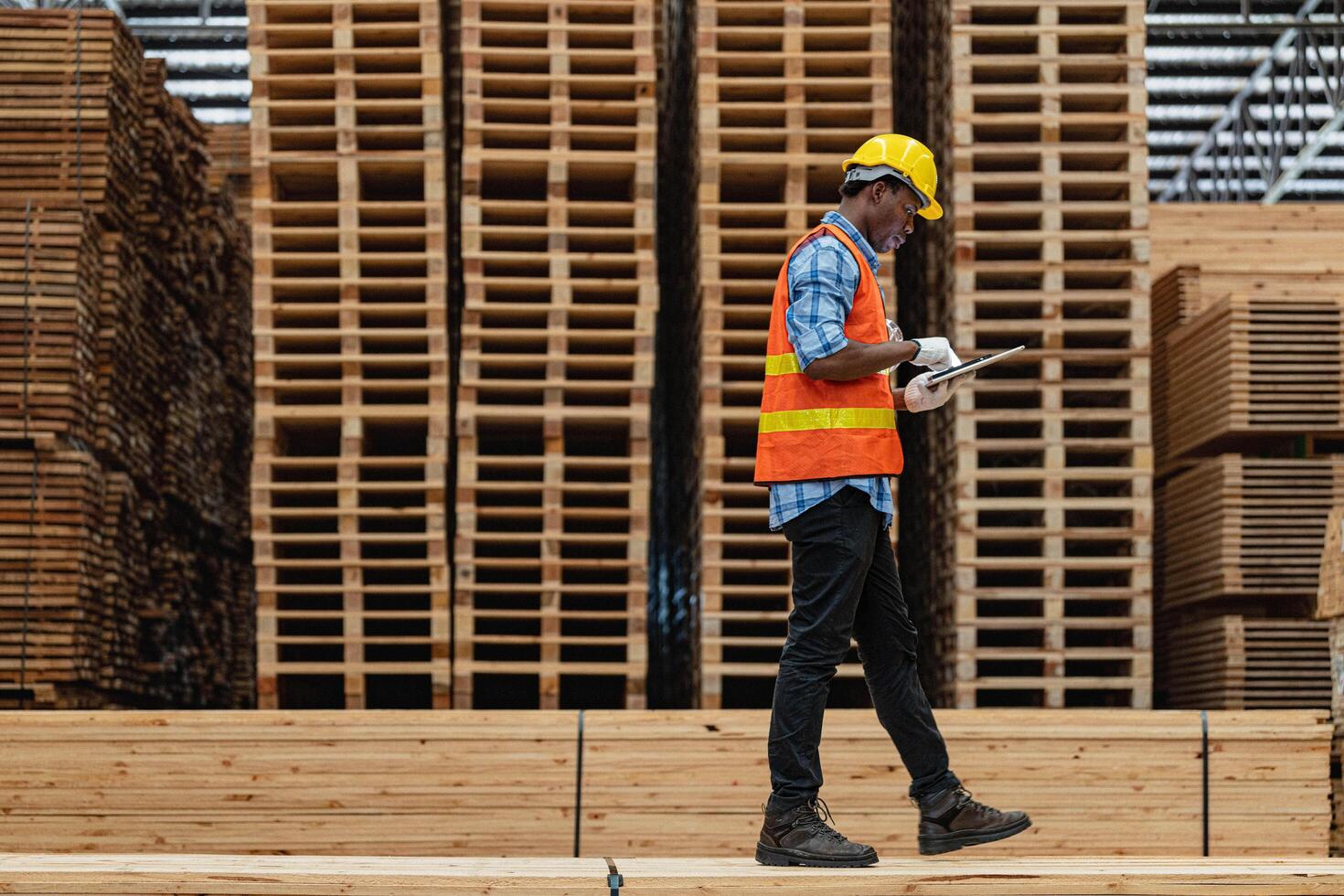 African workers man engineering walking and inspecting with working suite dress and hand glove in timber wood warehouse. Concept of smart industry worker operating. Wood factories produce wood palate. photo