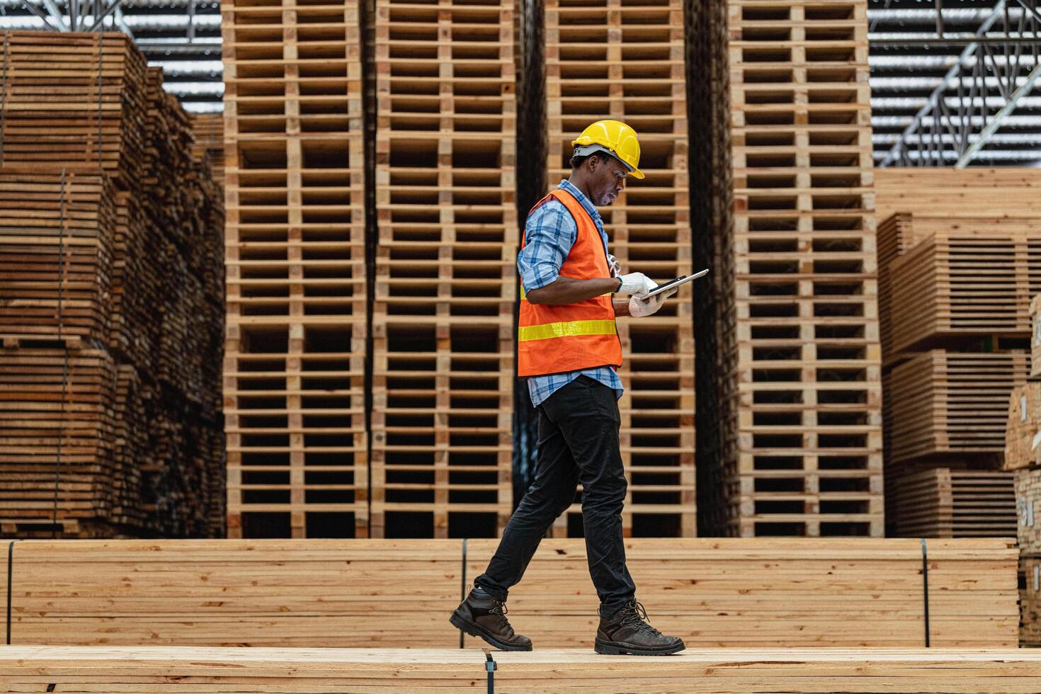 African workers man engineering walking and inspecting with working suite dress and hand glove in timber wood warehouse. Concept of smart industry worker operating. Wood factories produce wood palate. photo