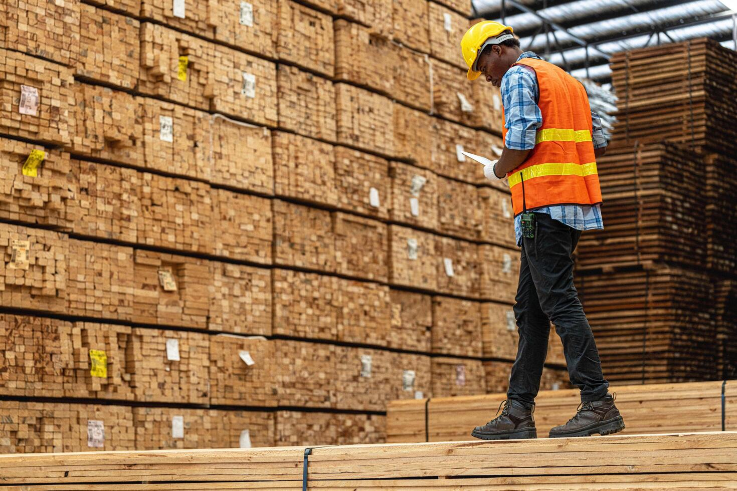 African workers man engineering walking and inspecting with working suite dress and hand glove in timber wood warehouse. Concept of smart industry worker operating. Wood factories produce wood palate. photo