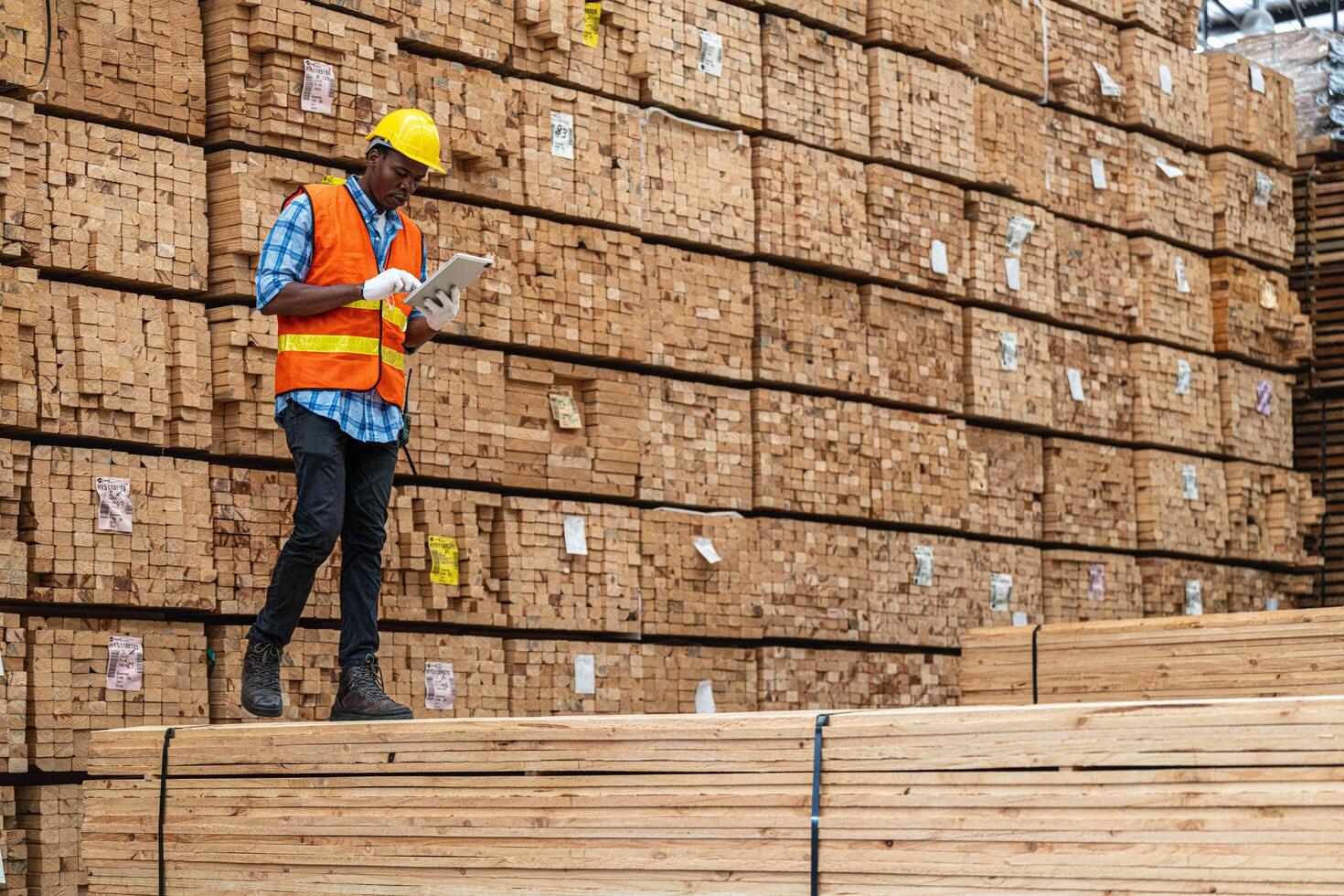 African workers man engineering walking and inspecting with working suite dress and hand glove in timber wood warehouse. Concept of smart industry worker operating. Wood factories produce wood palate. photo