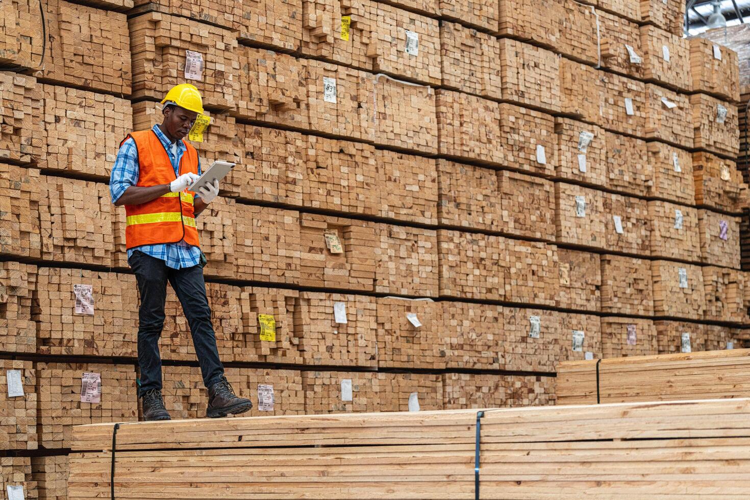 African workers man engineering walking and inspecting with working suite dress and hand glove in timber wood warehouse. Concept of smart industry worker operating. Wood factories produce wood palate. photo
