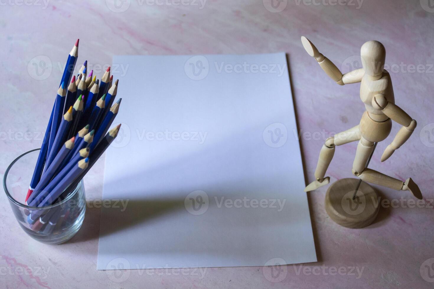 Colored pencils, empty paper and dummy for drawing on the table. photo