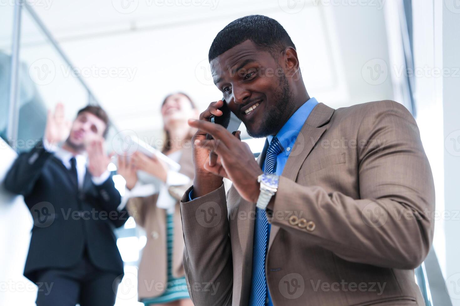 inteligente negro empresario acecho móvil teléfono. calvo adulto hombre vistiendo formal tener puesto. pensativo afroamericano empresario en un perfectamente a la medida traje en pie en escalera en oficina. foto