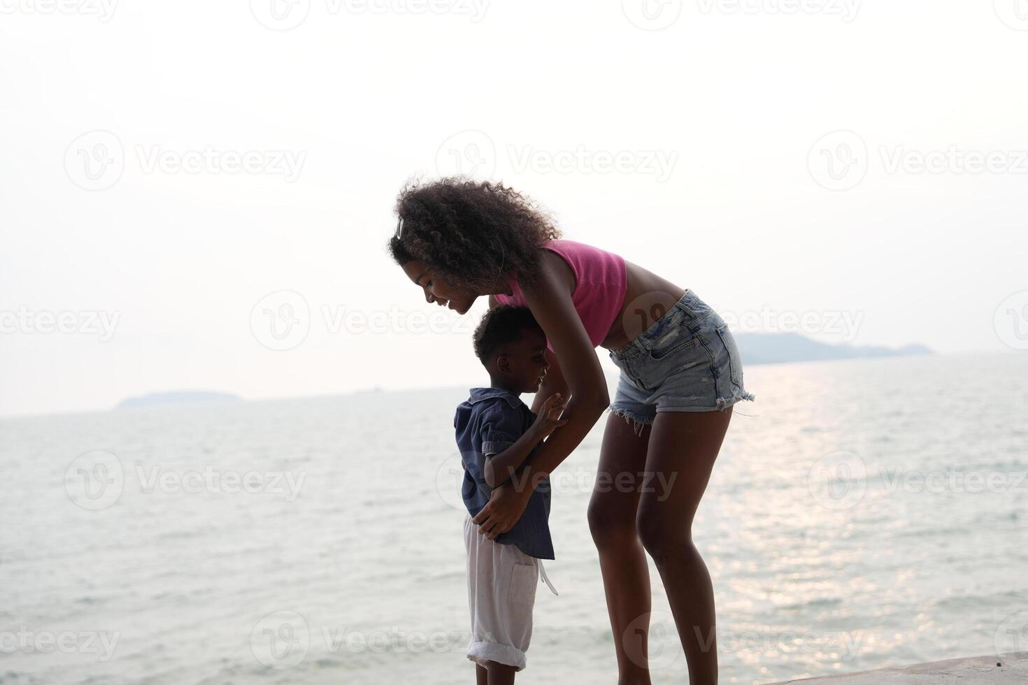 Mixed race African and Asian mother and boy is playing at the outdoor area. smiling happy family have fun running on the beach. portrait of mom and kid lifestyle with a unique hairstyle. photo