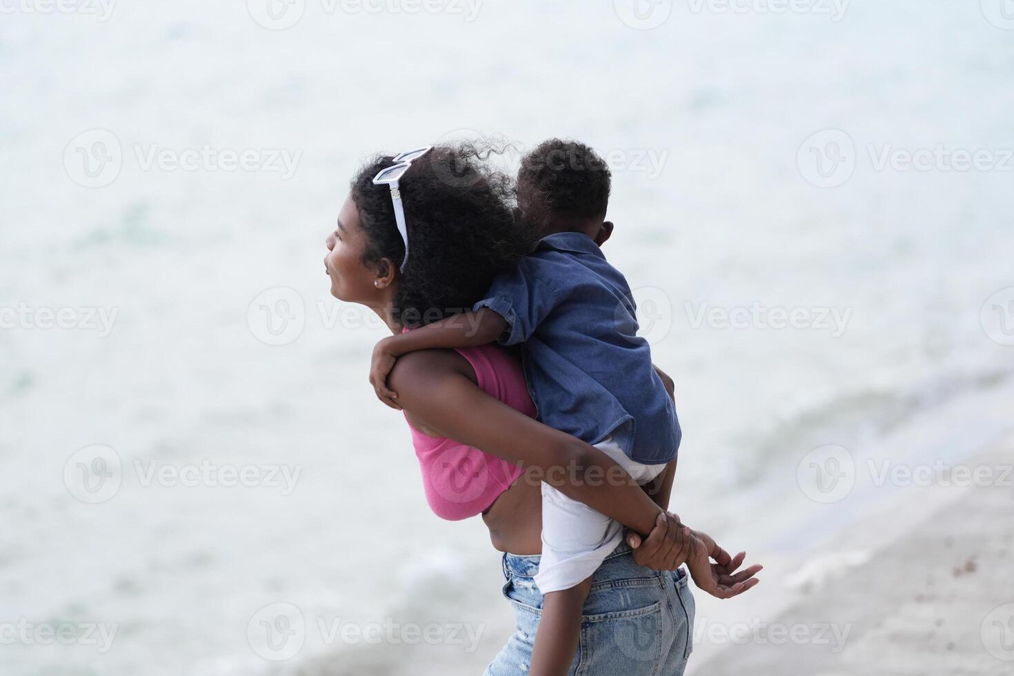 Mixed race African and Asian mother and boy is playing at the outdoor area. smiling happy family have fun running on the beach. portrait of mom and kid lifestyle with a unique hairstyle. photo
