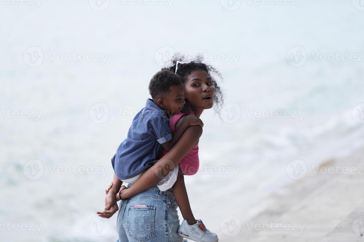 Mixed race African and Asian mother and boy is playing at the outdoor area. smiling happy family have fun running on the beach. portrait of mom and kid lifestyle with a unique hairstyle. photo