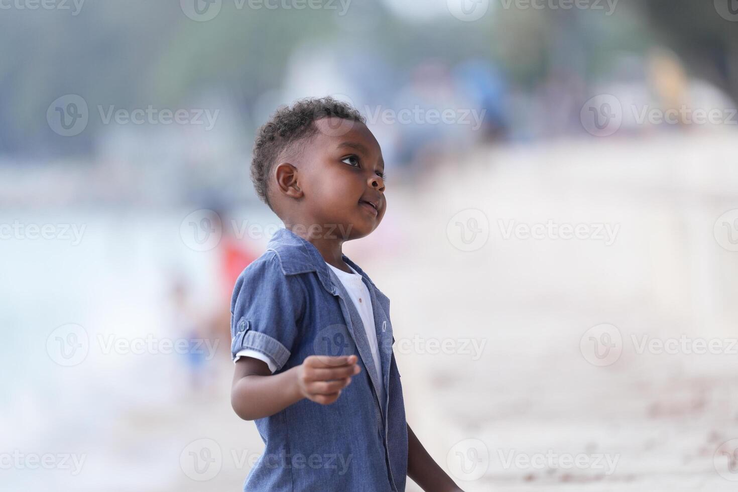 mezclado carrera africano y asiático chico es jugando a el al aire libre área. sonriente contento chico tiene divertido corriendo en el playa. retrato de chico estilo de vida con un único peinado. foto