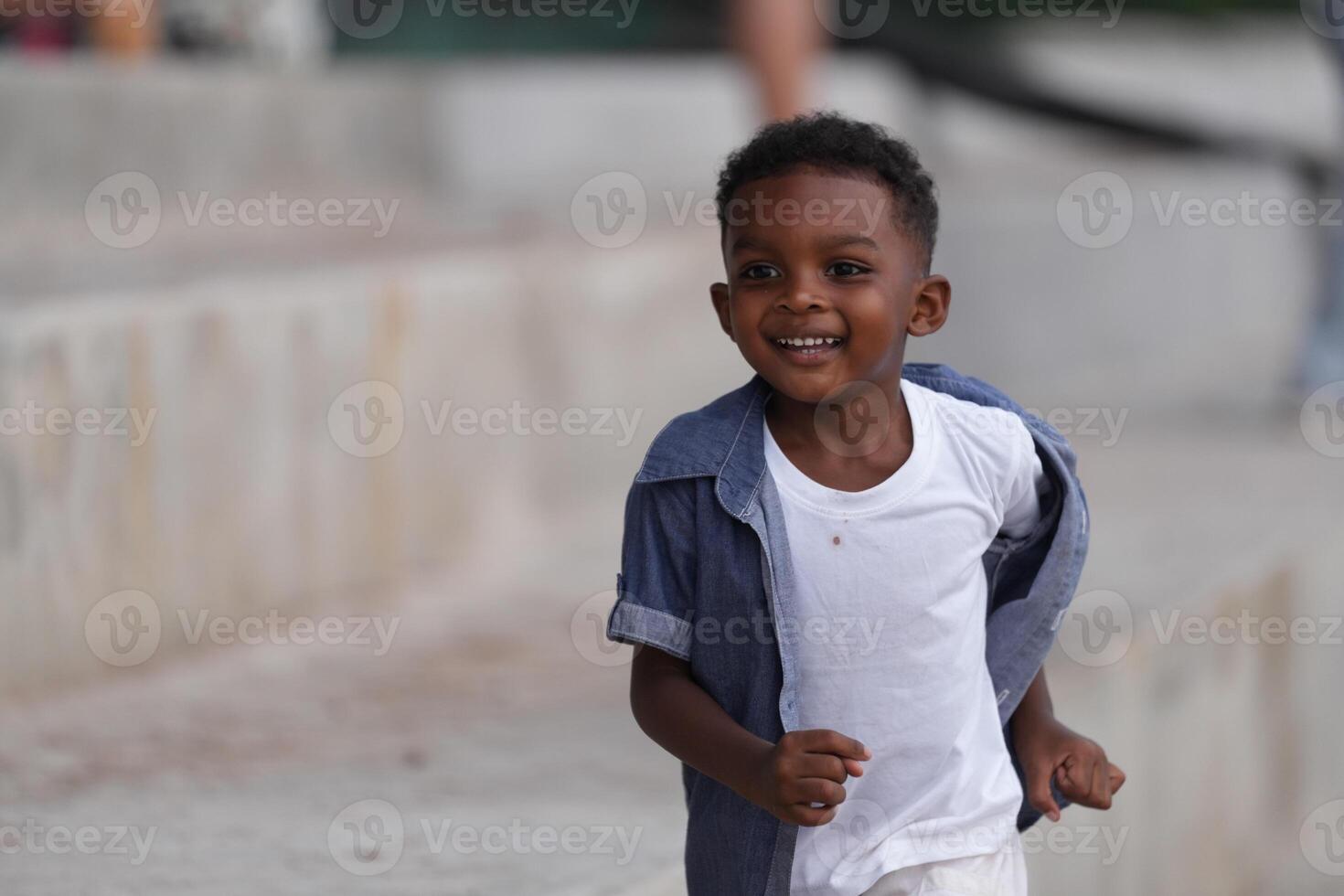 mezclado carrera africano y asiático chico es jugando a el al aire libre área. sonriente contento chico tiene divertido corriendo en el playa. retrato de chico estilo de vida con un único peinado. foto