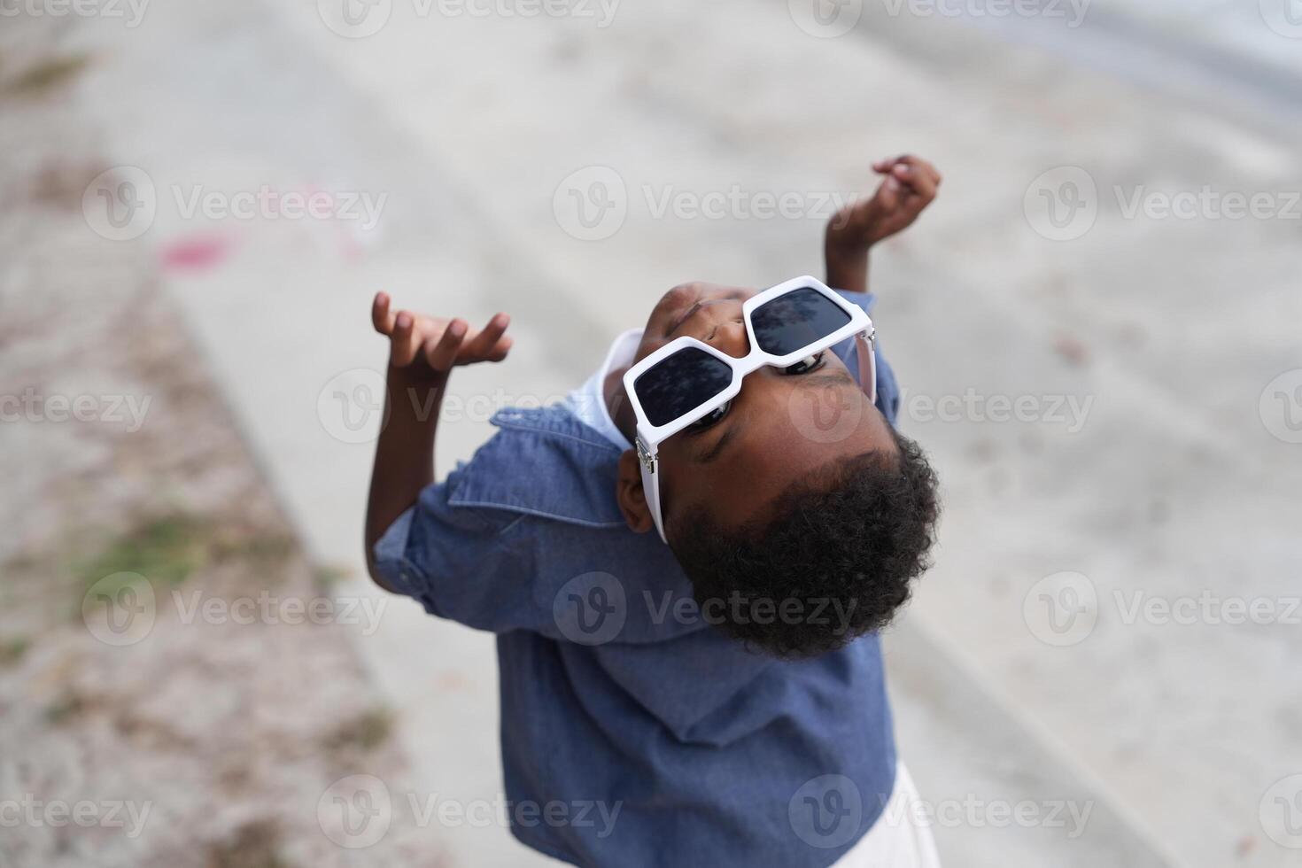 mezclado carrera africano y asiático chico es jugando a el al aire libre área. sonriente contento chico tiene divertido corriendo en el playa. retrato de chico estilo de vida con un único peinado. foto