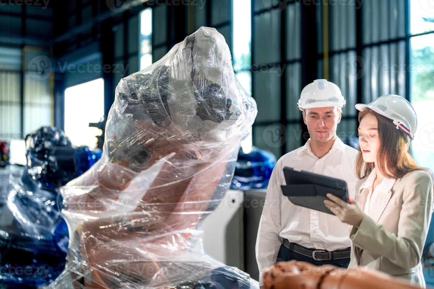 Sales manager and factory owner in suits negotiating selling robots used in the factory. Business engineers meeting and checking new machine robot. Workers walking at warehouse welding machine. photo
