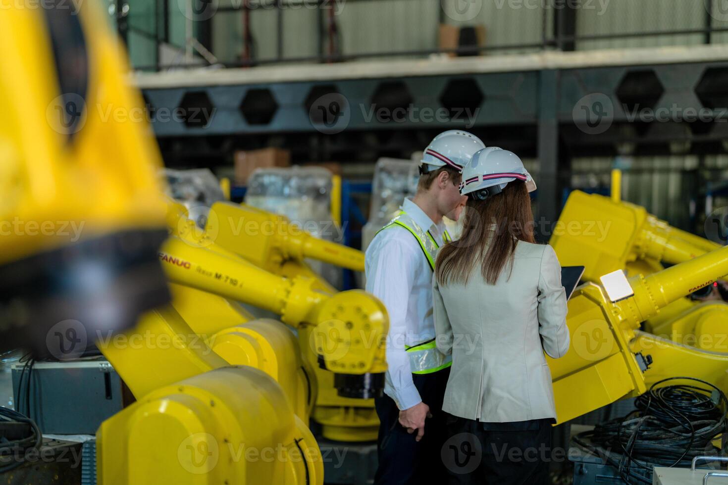 Factory engineers inspecting on machine with smart tablet. Worker works at heavy machine robot arm. The welding machine with a remote system in an industrial factory. Artificial intelligence concept. photo