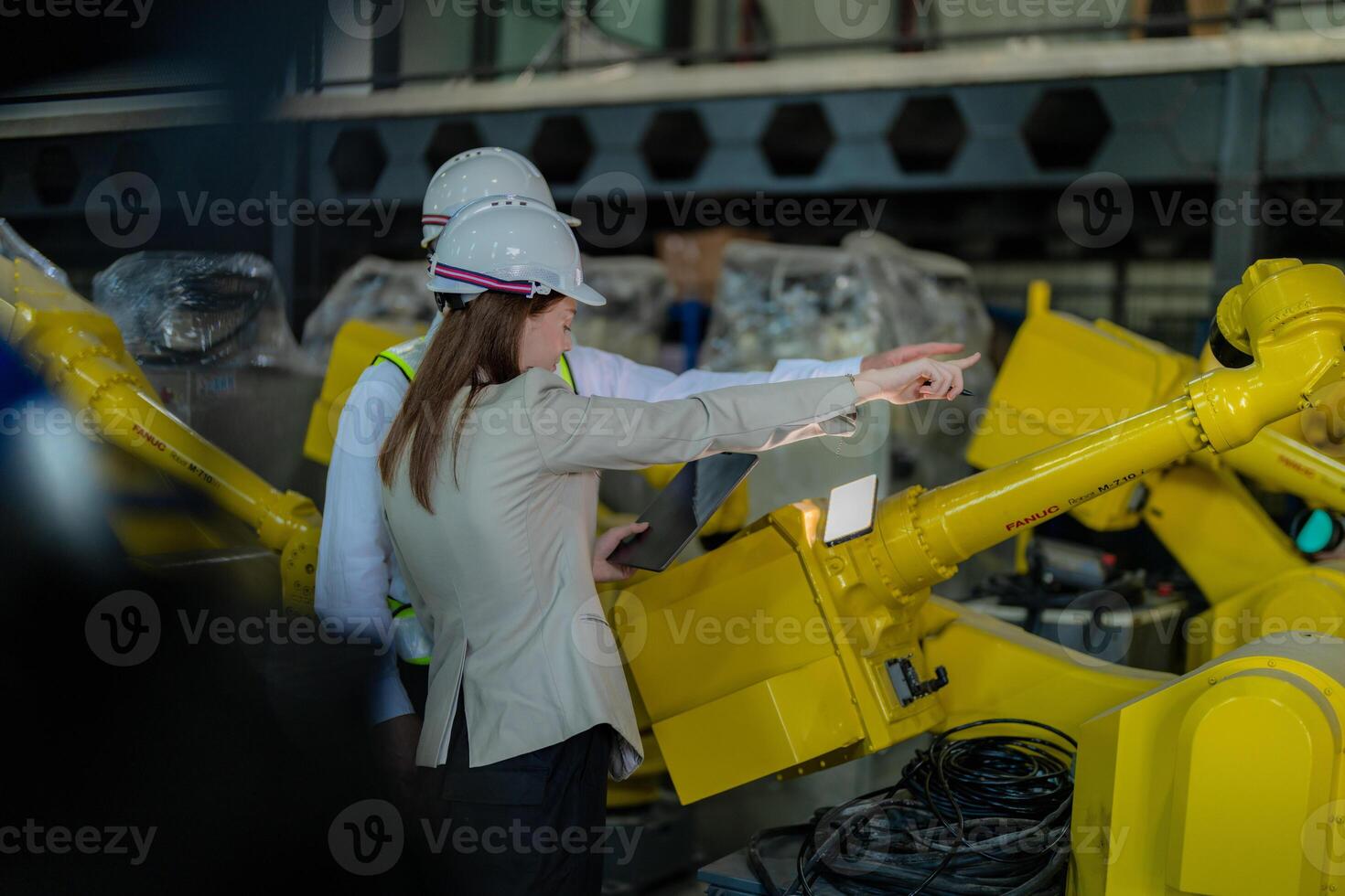 Factory engineers inspecting on machine with smart tablet. Worker works at heavy machine robot arm. The welding machine with a remote system in an industrial factory. Artificial intelligence concept. photo