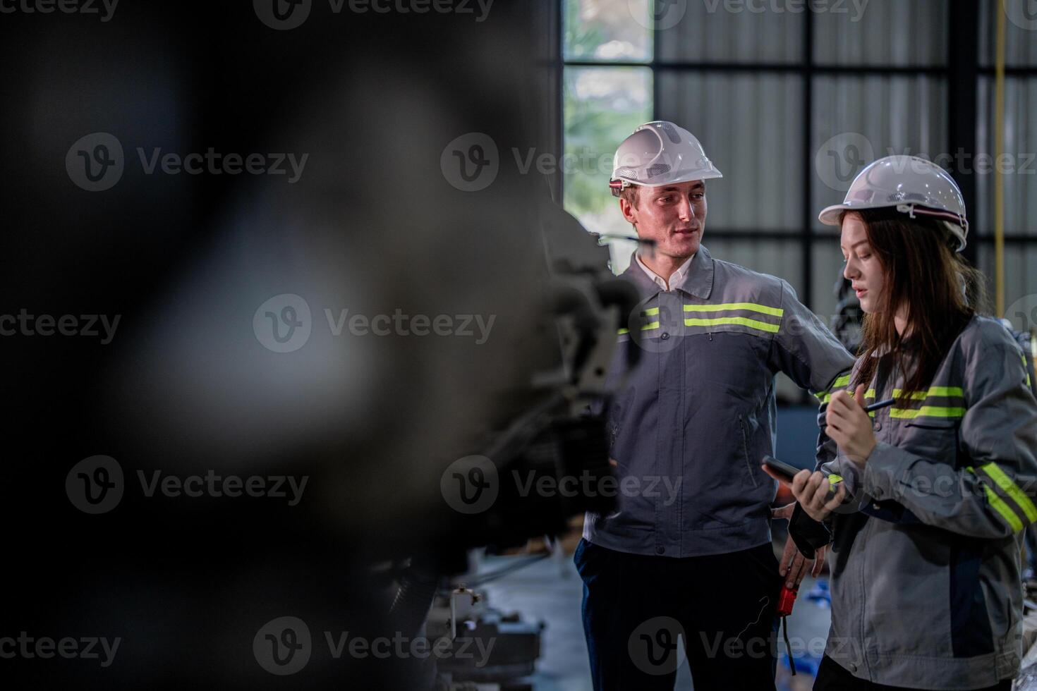 Factory engineer woman inspecting on machine with smart tablet. Worker works at machine robot arm. The welding machine with a remote system in an industrial factory. Artificial intelligence concept. photo