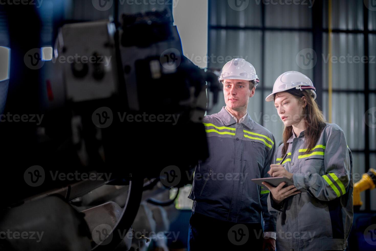 Factory engineer woman inspecting on machine with smart tablet. Worker works at machine robot arm. The welding machine with a remote system in an industrial factory. Artificial intelligence concept. photo