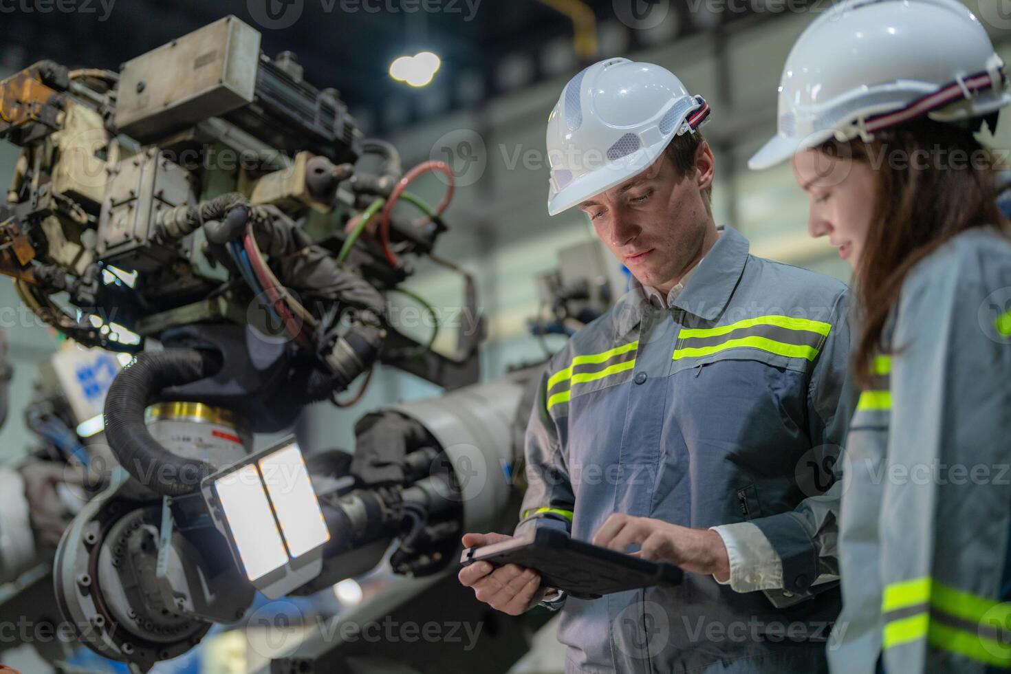 Factory engineer woman inspecting on machine with smart tablet. Worker works at machine robot arm. The welding machine with a remote system in an industrial factory. Artificial intelligence concept. photo