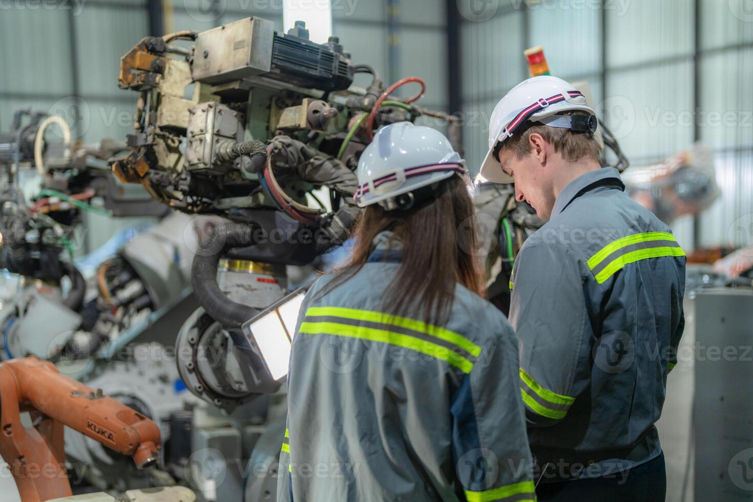 Factory engineer woman inspecting on machine with smart tablet. Worker works at machine robot arm. The welding machine with a remote system in an industrial factory. Artificial intelligence concept. photo