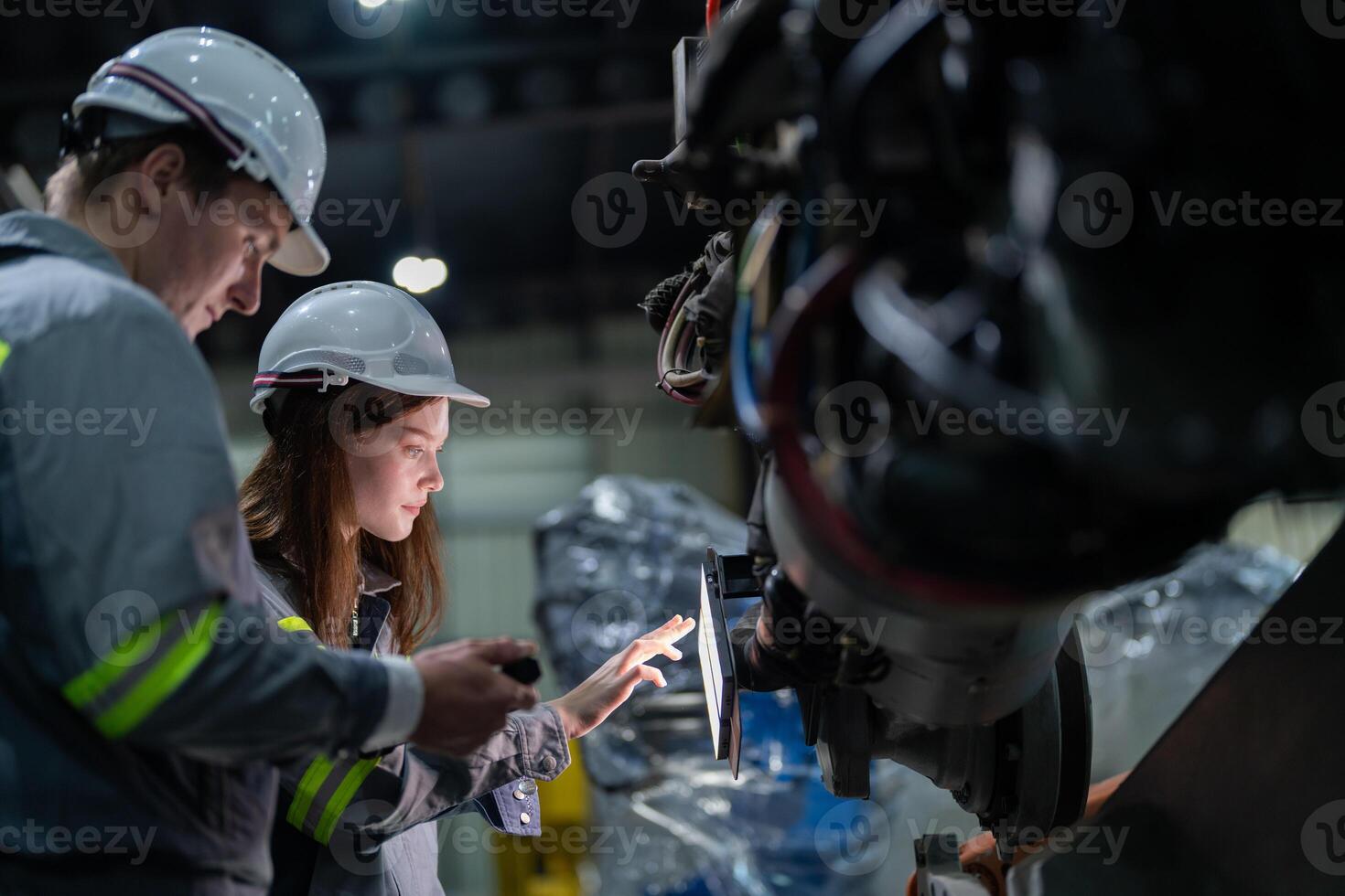 Factory engineer woman inspecting on machine with smart tablet. Worker works at machine robot arm. The welding machine with a remote system in an industrial factory. Artificial intelligence concept. photo