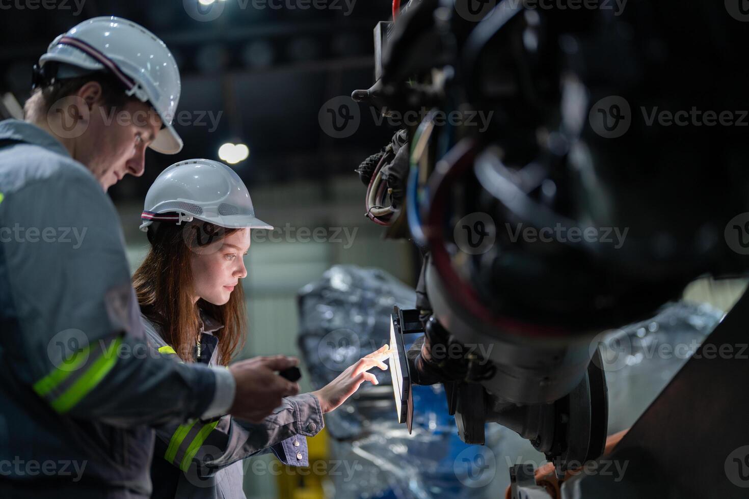 Factory engineer woman inspecting on machine with smart tablet. Worker works at machine robot arm. The welding machine with a remote system in an industrial factory. Artificial intelligence concept. photo