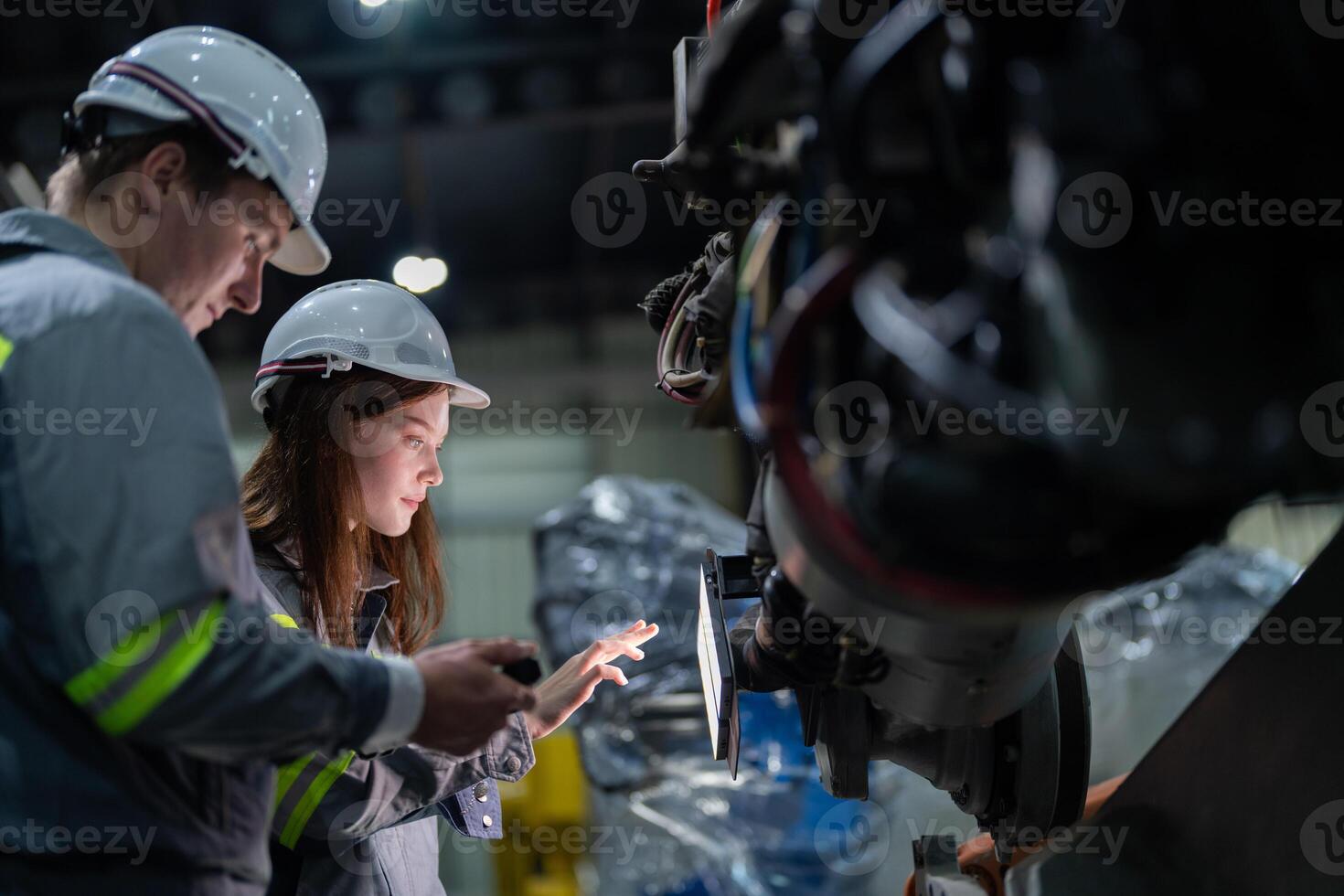 Factory engineer woman inspecting on machine with smart tablet. Worker works at machine robot arm. The welding machine with a remote system in an industrial factory. Artificial intelligence concept. photo